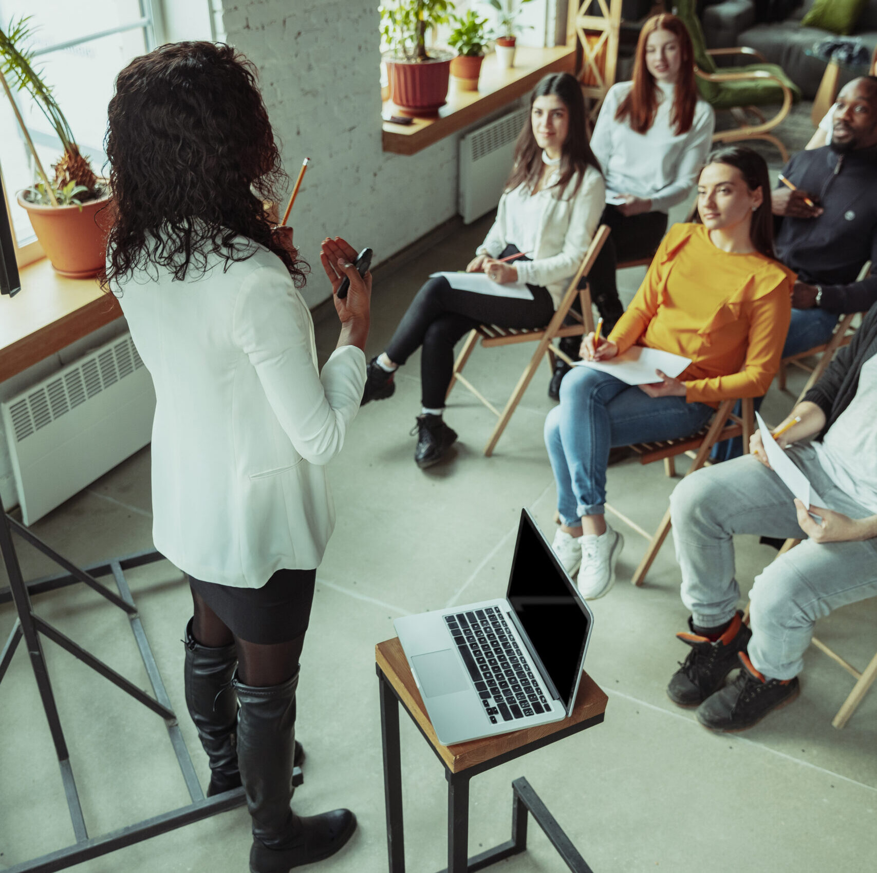 Female african-american speaker giving presentation in hall at workshop. Audience or conference hall. Rear view of participants in audience. Conference event, training. Education, diversity, inclusive concept.